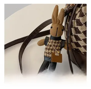 Detail of bunny plush charm on a houndstooth pattern bucket bag with gold chain