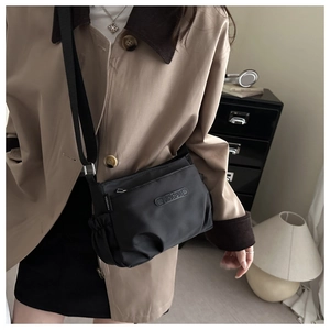 Detail of minimalist black nylon crossbody bag with rubberized logo and wide strap