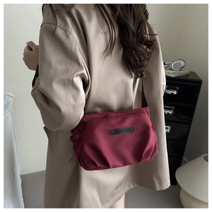 Detail of burgundy nylon crossbody bag with zipper pocket and JINGPIN logo on trench coat