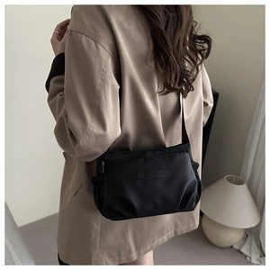 Detail of black pleated nylon shoulder bag with silk sheen on a beige blazer