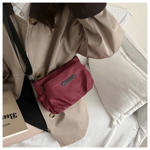 Detail of burgundy ruched crossbody bag with black logo patch and nylon texture