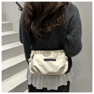 Detail of a creamy white nylon crossbody bag with JINGPIN logo and pleated side design