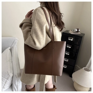Détail du sac cabas en cuir marron foncé avec lettrage doré sur un manteau en laine