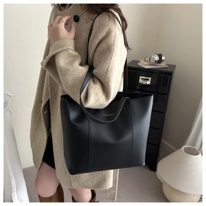 Détail du cabas en cuir noir avec lettrage doré porté sur un manteau en laine beige
