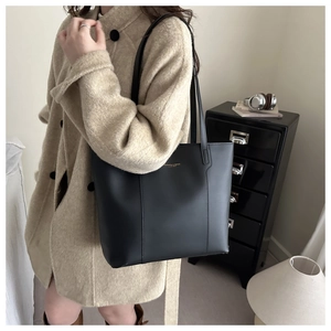 Détail d'un grand sac cabas en cuir noir avec lettrage doré et fines bretelles en cuir