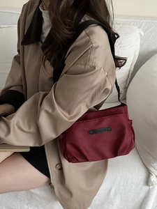 Elegant burgundy pleated nylon shoulder bag with logo detail worn over a khaki trench coat