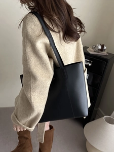Grand sac fourre-tout élégant en cuir noir porté à l'épaule dans un intérieur minimaliste
