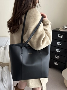Sac fourre-tout en cuir noir mat avec lettrage doré porté par un mannequin en intérieur