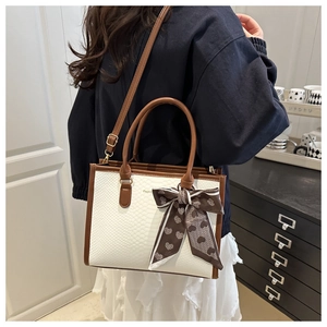 Dettaglio della borsa tote pitonata bianca con manici marroni e accessorio foulard a cuori