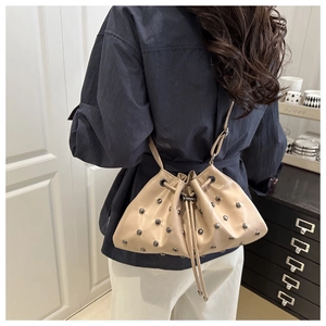 Detail of beige rivet drawstring bucket bag with silver studs and polished faux leather