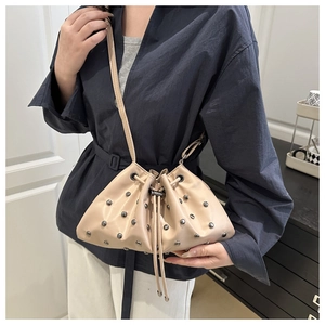 Detail of beige bucket bag with silver studs and drawstring closure on blue shirt