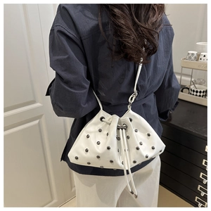 Detail of white drawstring bucket bag featuring silver rivet studs and a long leather strap