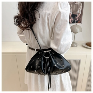 Detail of black drawstring bucket bag with silver studs worn by model in minimalist room