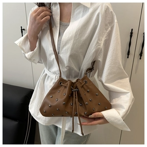 Detail view of brown leather bucket bag with silver rivets and drawstring closure