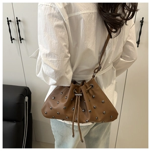 Brown leather bucket bag with silver studs and drawstring detail worn by a model