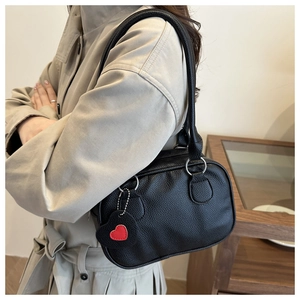 Detail of black lychee grain leather shoulder bag with decorative red heart charm