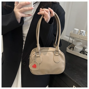 Dettaglio della borsa beige in pelle martellata con un ciondolo a cuore rosso sul lato