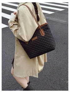 Close-up of black quilted tote bag with brown leather trim and shoulder straps on street