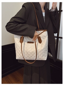 Detail of white quilted tote bag featuring brown leather straps on a model in a black suit