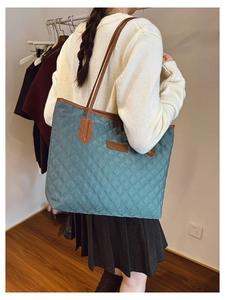 Quilted teal tote bag with brown leather handles worn by a model in a cozy room