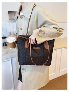 Detail of quilted tote bag with brown leather handles and a fashion brand logo patch