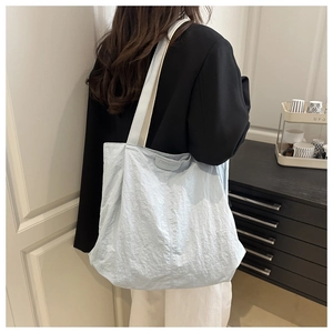 Detail of light blue pleated tote bag with FASHION leather tag on textured fabric surface