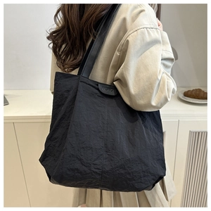Detail of black large-capacity tote bag with pleated nylon texture and leather strap