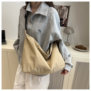 Sac à bandoulière en toile beige porté par un mannequin dans un décor minimaliste