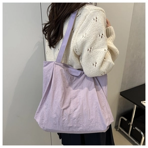 Detail of purple pleated tote bag with fashion label and long shoulder strap on model