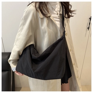 Detail view of large black nylon dumpling bag worn over a beige trench coat for casual style