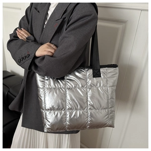 Detail of silver quilted tote bag with black straps worn over a grey casual blazer