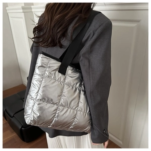 Close-up of metallic silver quilted tote bag with wide black shoulder straps and padded texture