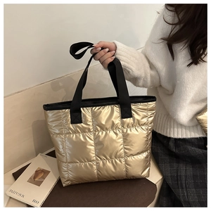 Detail der goldfarbenen Stepptasche mit schwarzen gewebten Griffen und Stoffstruktur
