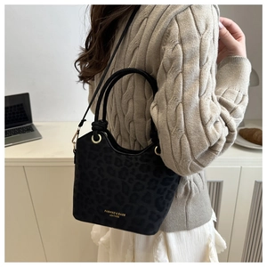 Detail of black leopard print bucket bag with gold hardware on a chic beige knit outfit