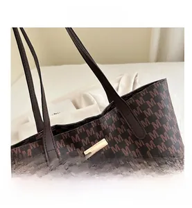 Detailed macro view of dark brown tote bag with M-pattern print and gold metal buckle