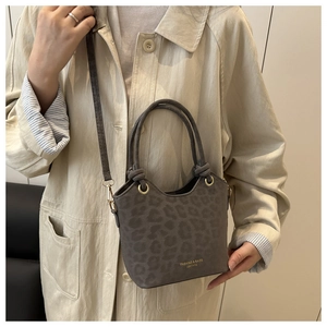 Detail of grey leopard print bucket bag with knot handle and gold hardware on beige coat