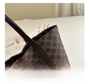 Detail view of brown tote bag with M-pattern print and smooth leather handle strap