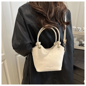 Detail of cream leather bucket bag with knotted handles and elegant gold lettering