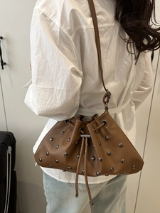 Brown leather drawstring bucket bag with silver studs worn by model over shoulder