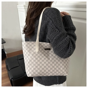 Detail view of beige monogram tote bag worn with a casual autumn knit sweater