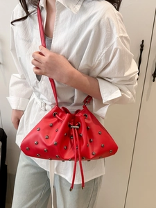 Red drawstring bucket bag with silver studs and slim crossbody strap on model