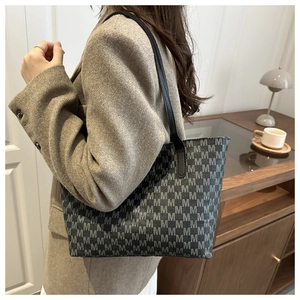 Detail of dark grey tote bag with M-pattern print worn over a brown wool blazer