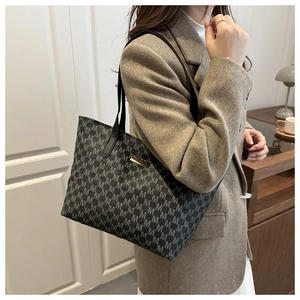 Detail of grey tote bag with M-pattern logo worn with a brown wool blazer
