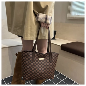 Close-up of a stylish brown tote bag featuring a repeating M pattern and gold plaque.