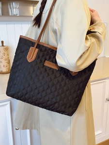 Black quilted tote bag with brown leather trim shown on shoulder for daily commute use