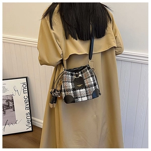 Detail of tweed bucket bag with rabbit charm and leather base on a female model