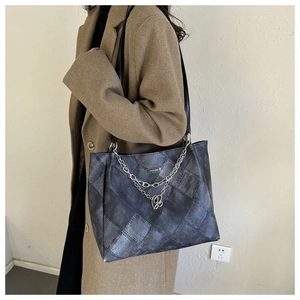 Detail of dark grey quilted tote bag with silver chain and heart pendant accessory
