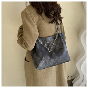 Detail of dark grey quilted tote bag with silver chain and heart pendant on coat