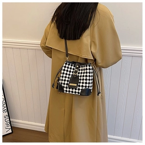 Detail of checkered bucket bag with drawstring and leather strap on khaki trench coat