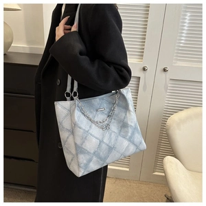 Detail of light blue quilted tote bag with silver chain and 'B' pendant on model
